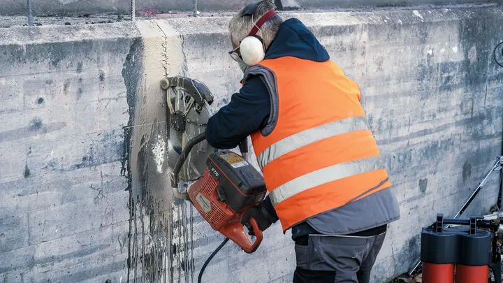 En person med säkerhetsutrustning använder en motorsåg för att såga igenom en betongvägg.