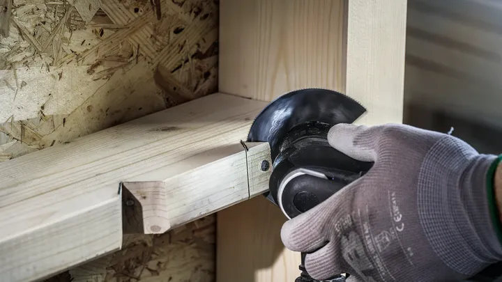 En person som bär säkerhetsutrustning sågar träbjälkar med en vinkelslip.