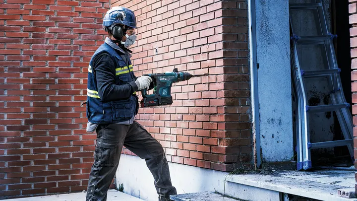 En person med säkerhetsutrustning borrar in i en tegelvägg nära en dörröppning.