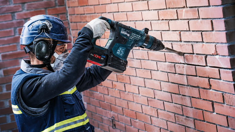 En person med säkerhetsutrustning borrar in i en tegelvägg.