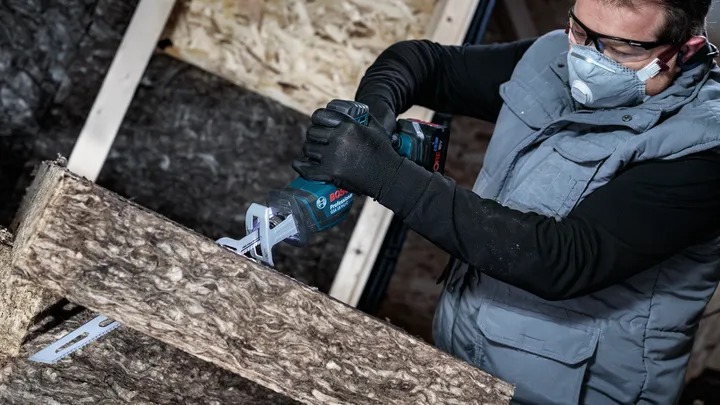 En person med säkerhetsutrustning sågar isoleringsmaterial med en tigersåg.