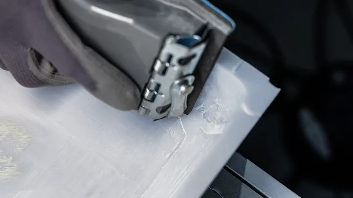 En person som bär säkerhetsutrustning använder ett elverktyg för att skära en plastfolie.