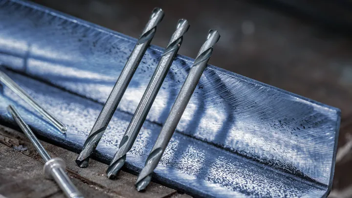 Tre metallborrar vilar på en blå stålvinkel på en arbetsbänk.