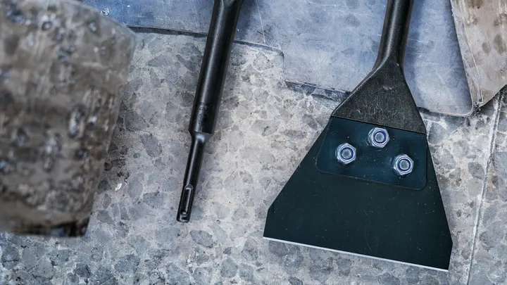 Bred metallmejsel med bultar placerade på en texturerad stenyta.