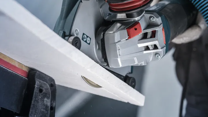 En person som bär säkerhetsutrustning sågar en kakelplatta med en handhållen kapmaskin.