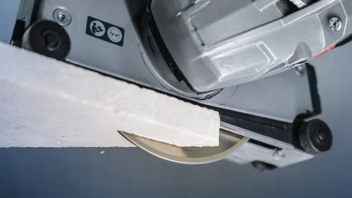 Cirkelsågblad som skär igenom en bit vitt konstruktionsmaterial.