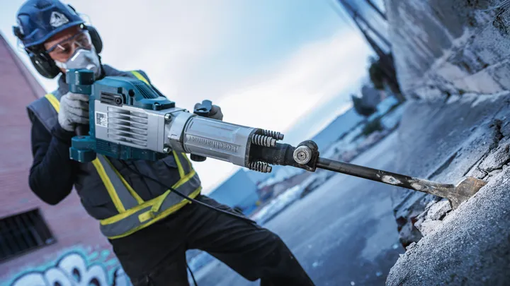 En person som bär säkerhetsutrustning använder ett rivningsverktyg för att bryta betong.