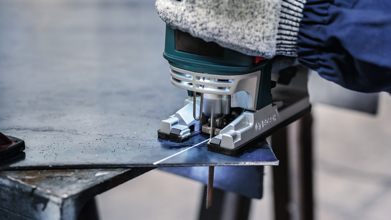 En person med säkerhetsutrustning sågar en metallplåt med en sticksåg.