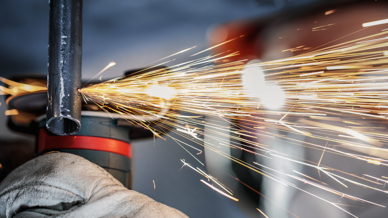 En person med säkerhetsutrustning slipar ett metallrör, vilket producerar ljusa gnistor.