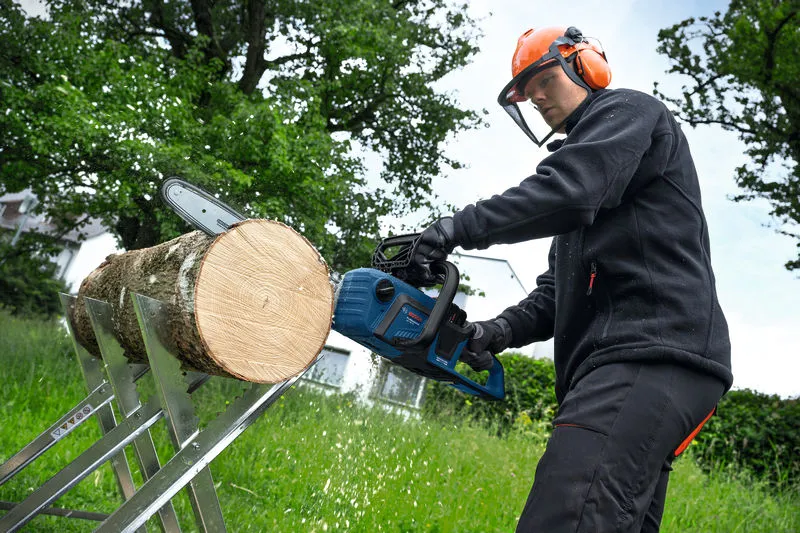 En person med säkerhetsutrustning använder en sladdlös motorsåg för att såga en stock utomhus.