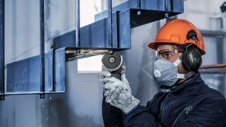 En person med säkerhetsutrustning slipar en metallbalk, vilket producerar gnistor.