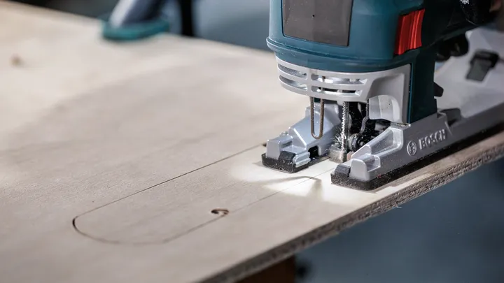 Sticksåg sågar en rektangulär form i en plywoodskiva.