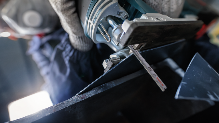 En person som bär säkerhetsutrustning sågar metall med en sticksåg.