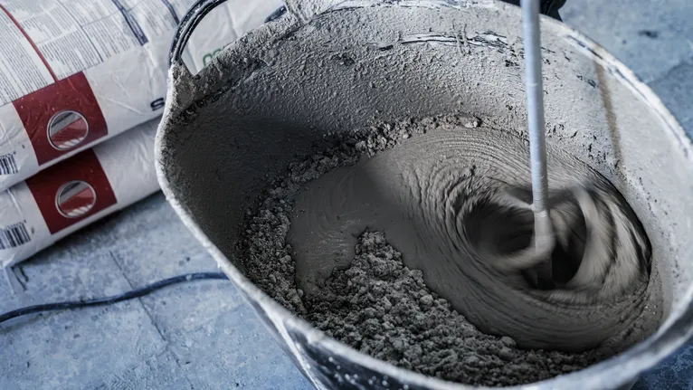 Elektrisk mixer som blandar cementpulver i en stor svart hink på en byggarbetsplats.