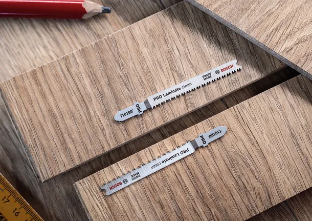 Två sticksågsblad placerade på laminatskivor med en penna och linjal i närheten.