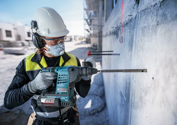 En person med säkerhetsutrustning borrar in i en betongvägg på en byggarbetsplats.