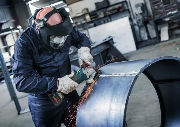 En person med säkerhetsutrustning slipar kanten på ett stort metallrör, vilket producerar gnistor.