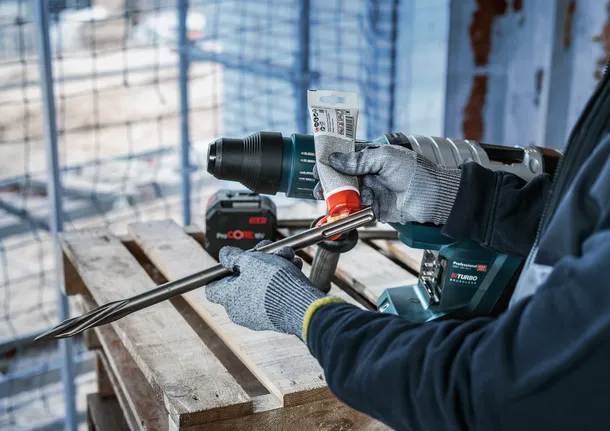 En person som bär säkerhetsutrustning applicerar smörjmedel på ett stort borr.