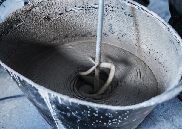 Ett blandningsverktyg rör om cement i en stor svart hink.