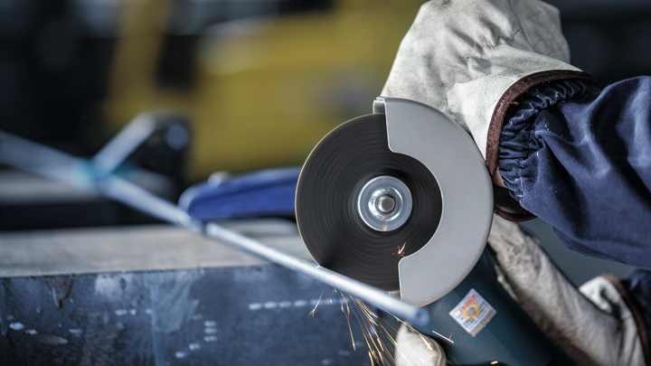 En person som bär säkerhetsutrustning skär metallrör med en vinkelslip.