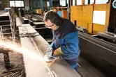 En person med säkerhetsutrustning slipar en metallbalk, vilket producerar gnistor.