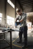 En person med säkerhetsutrustning borrar i en metallbalk i en verkstad.