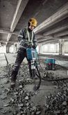 En person med säkerhetsutrustning använder en hammare för att riva betonggolv.