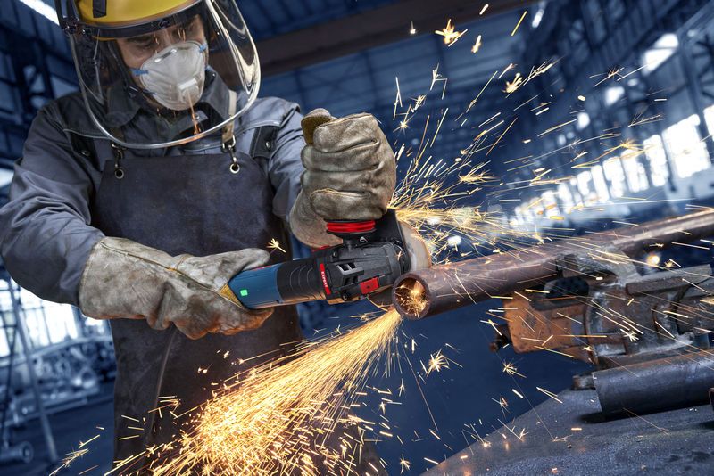 En person med säkerhetsutrustning slipar ett metallrör i en industriell verkstad.