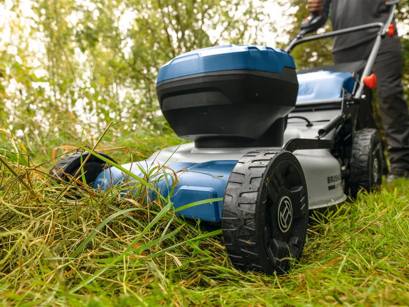 En person använder en sladdlös gräsklippare över högt gräs utomhus.