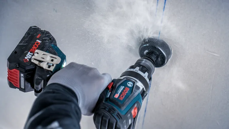 En person med säkerhetsutrustning borrar ett hål i en vägg med ett elverktyg.
