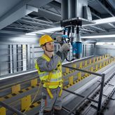 En person med säkerhetsutrustning använder en magnetkärnborr på en stålbalk.