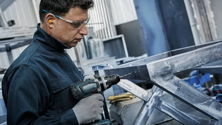 En person med säkerhetsutrustning borrar i en metallram.