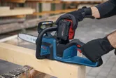 En person med säkerhetsutrustning installerar ett batteri i en sladdlös motorsåg på en träbalk.