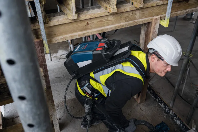 En person med säkerhetsutrustning använder en betongvibrator på en byggarbetsplats.