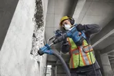 En arbetare med säkerhetsutrustning använder en borrhammare för att borra i en betongvägg.
