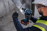En person som bär säkerhetsutrustning använder en sladdlös slagnyckel på en metallbalk.
