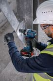 En person som bär säkerhetsutrustning använder en sladdlös slagnyckel på en metallbalk.