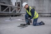 En person som bär säkerhetsutrustning använder en sladdlös slagnyckel för att fästa en bult i betong.