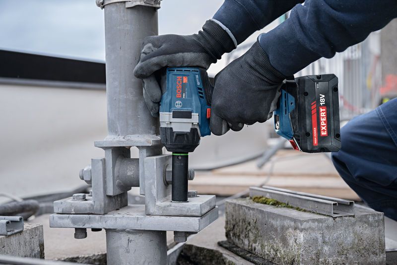 En person som bär säkerhetsutrustning använder en sladdlös slagnyckel på ett metallstöd.