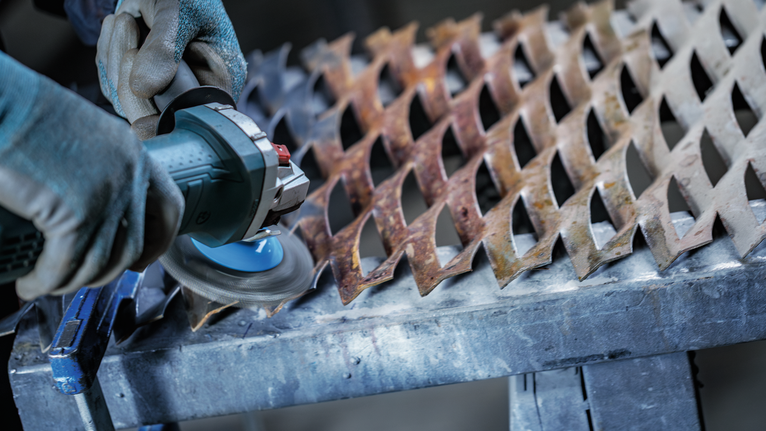 En person med säkerhetsutrustning slipar ett rostigt metallgaller med en vinkelslip.