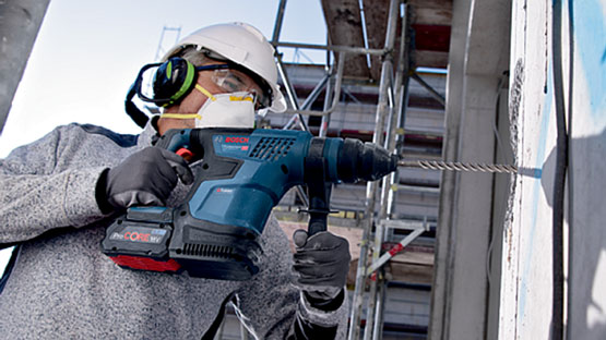 Delavec v čeladi uporablja Bosch Professional udarni vrtalnik na gradbišču.