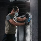 Oseba, ki nosi varnostno opremo, uporablja kotni brusilnik na betonski steni.