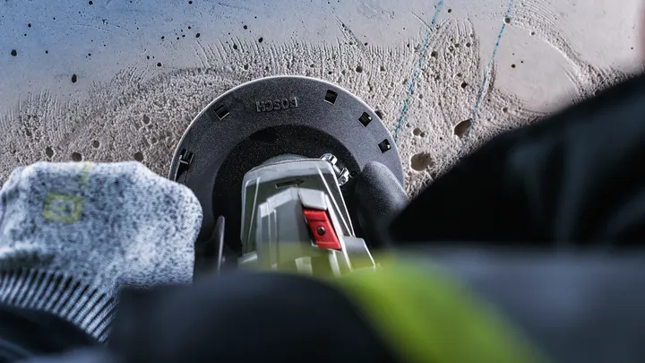 Delavec v varnostni opremi vrta v beton z električnim orodjem.