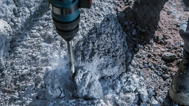 Kladivo vrtalnik prebija hrapav beton, delavec nosi zaščitno opremo.