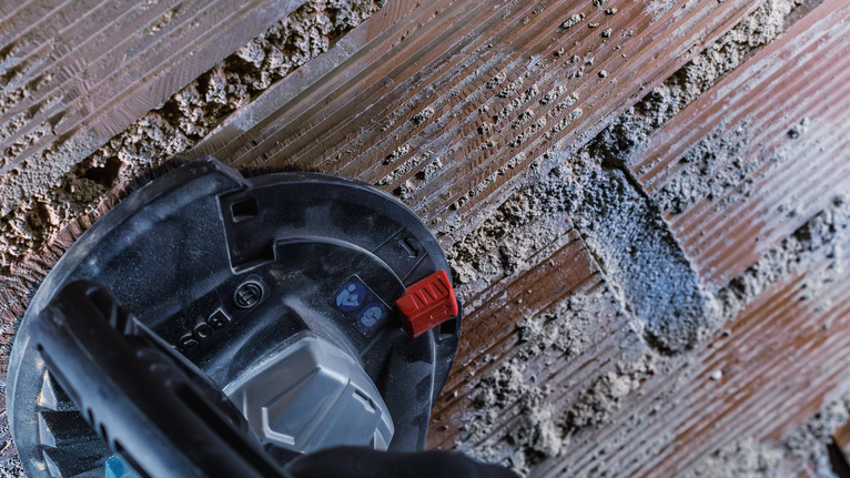 Oseba, ki nosi varnostno opremo, v betonsko steno vreže kanal.