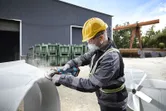 Oseba v zaščitni opremi brusi kovino na prostem na industrijskem območju.