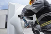 Oseba v zaščitni opremi brusi rob velike kovinske cevi na prostem.