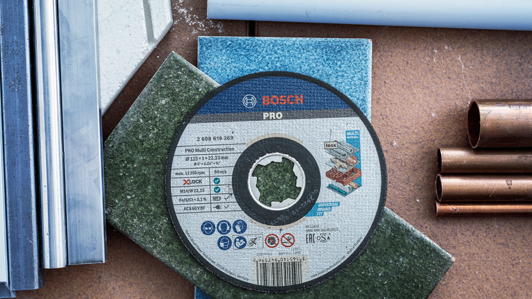 Rezalni disk, nameščen na barvnih ploščicah, obdan s kovinskimi in plastičnimi cevmi.