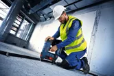 Delavec v varnostni opremi pritrdi cev na betonska tla z akumulatorskim žebljalnikom za beton.