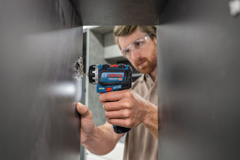 Oseba, ki nosi varnostno opremo, z izvijačem namesti tečaj omare.